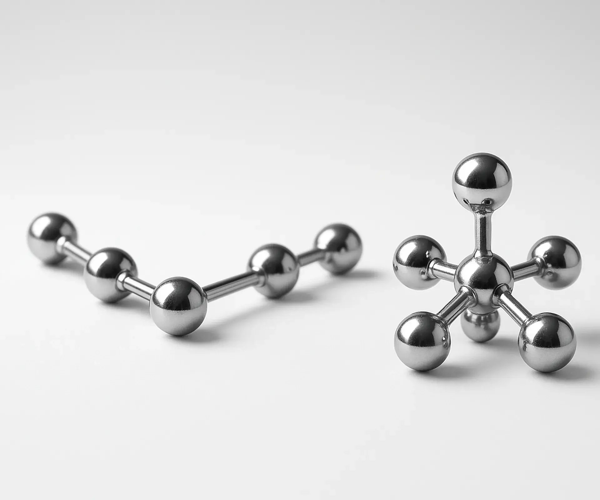 Two chrome ball-and-stick molecule models, one long chain and one compact, side by side on white