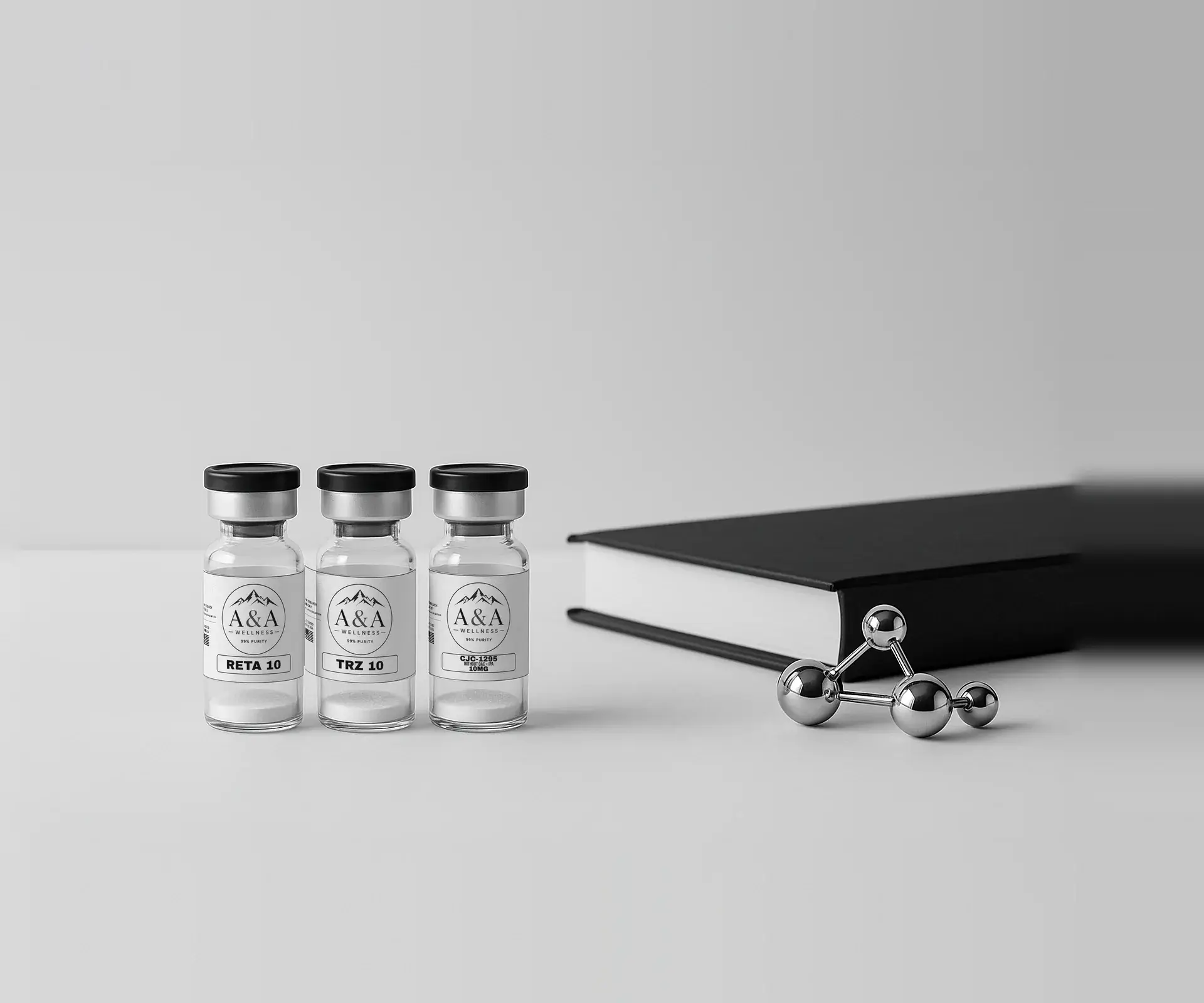 Three A&A Wellness research vials, a black reference book and a chrome molecule model on a white surface