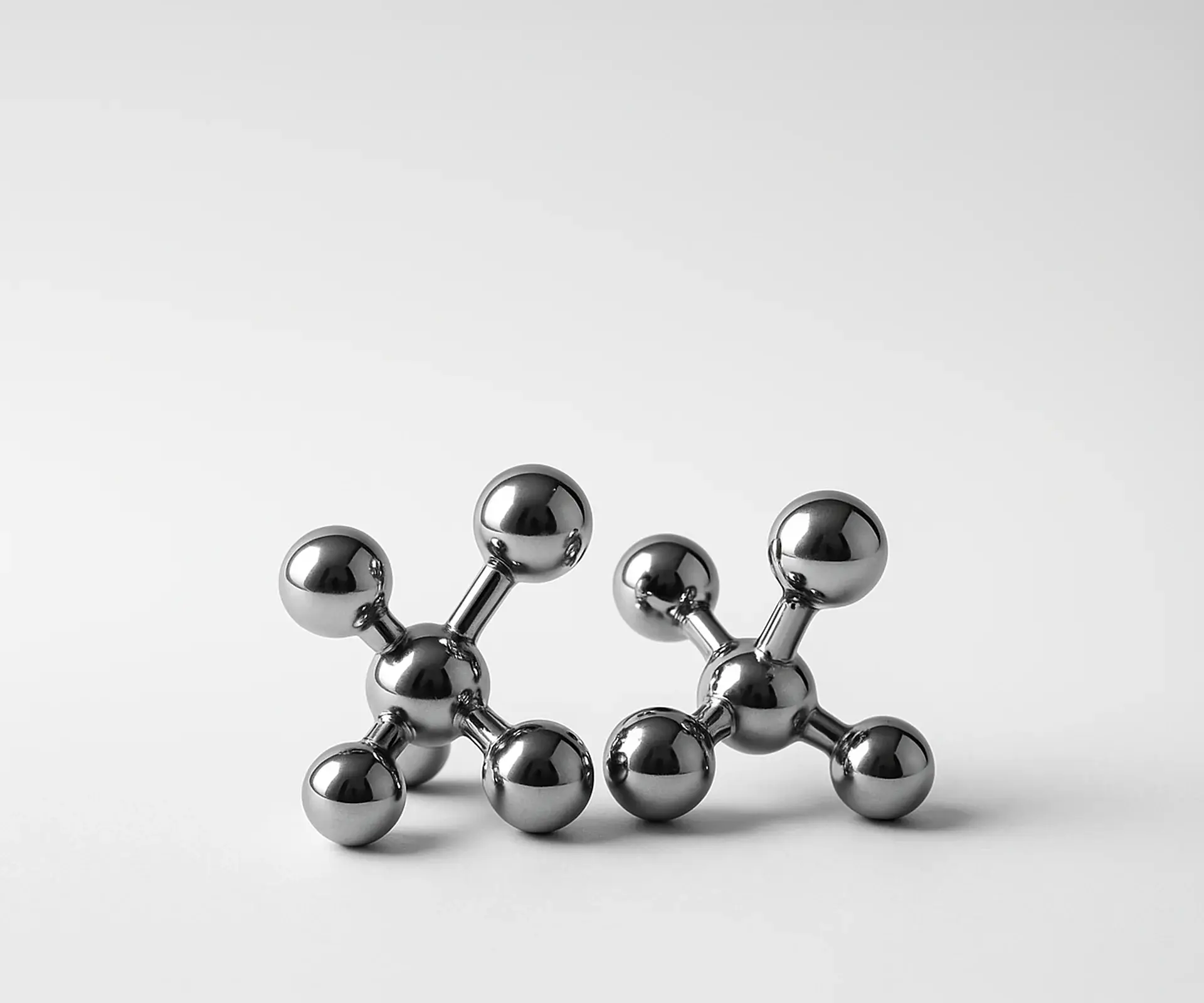 Two chrome ball-and-stick molecule models side by side on a white surface