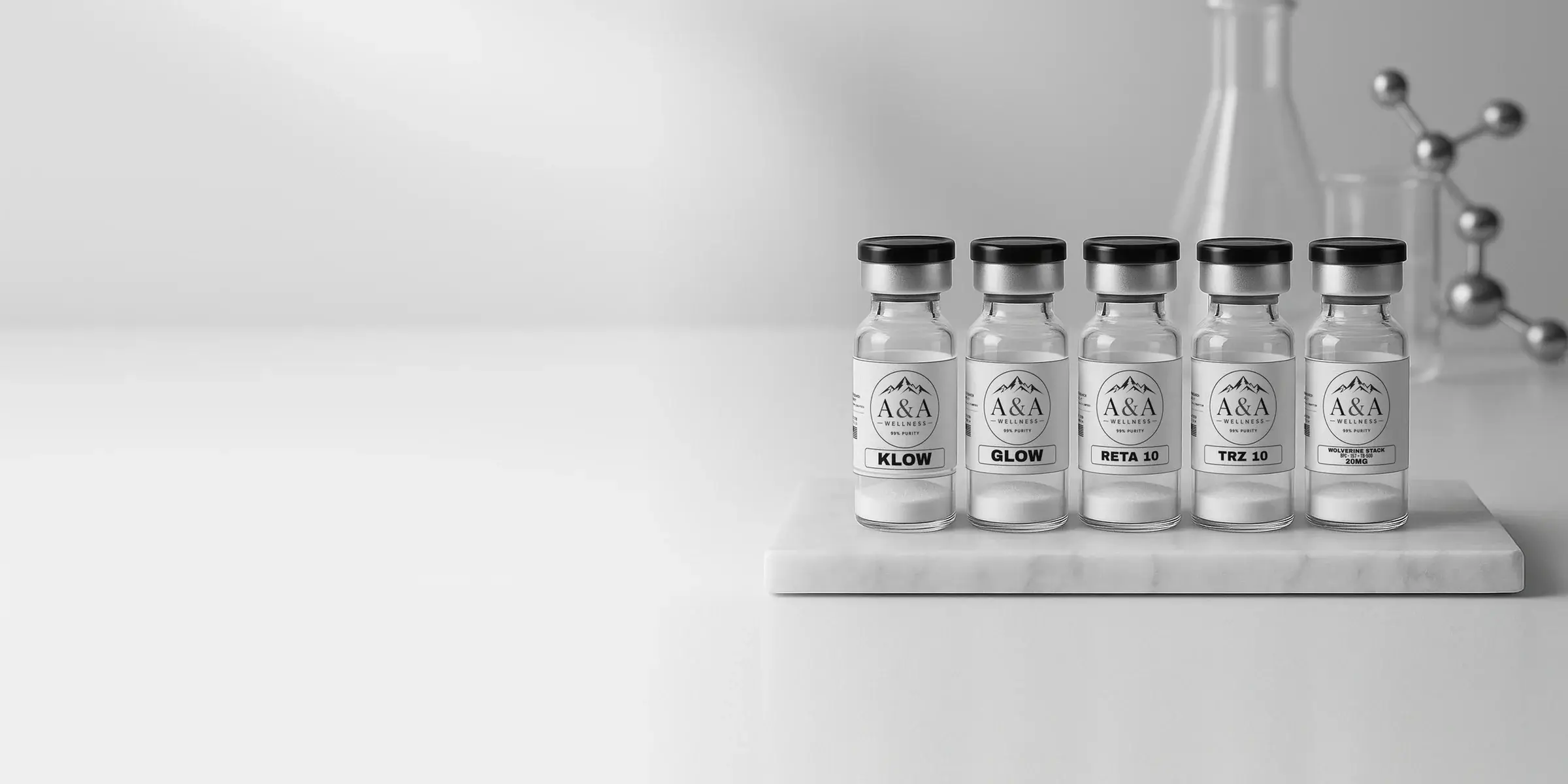 Five A&A Wellness research vials on a white marble riser at the right, with lab glassware and a chrome molecule model softly blurred behind and open light space to the left