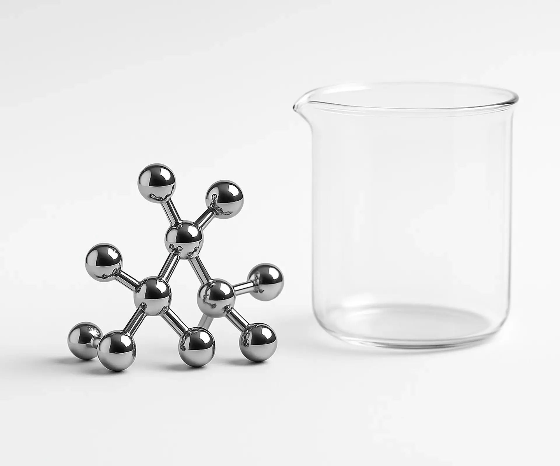 Chrome ball-and-stick molecule model beside a clear glass beaker on a white bench