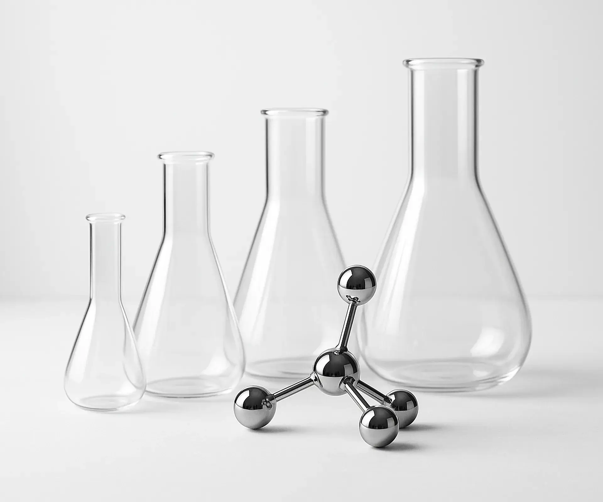 Clear glass flasks of varying sizes with a chrome molecule model in front on a white bench